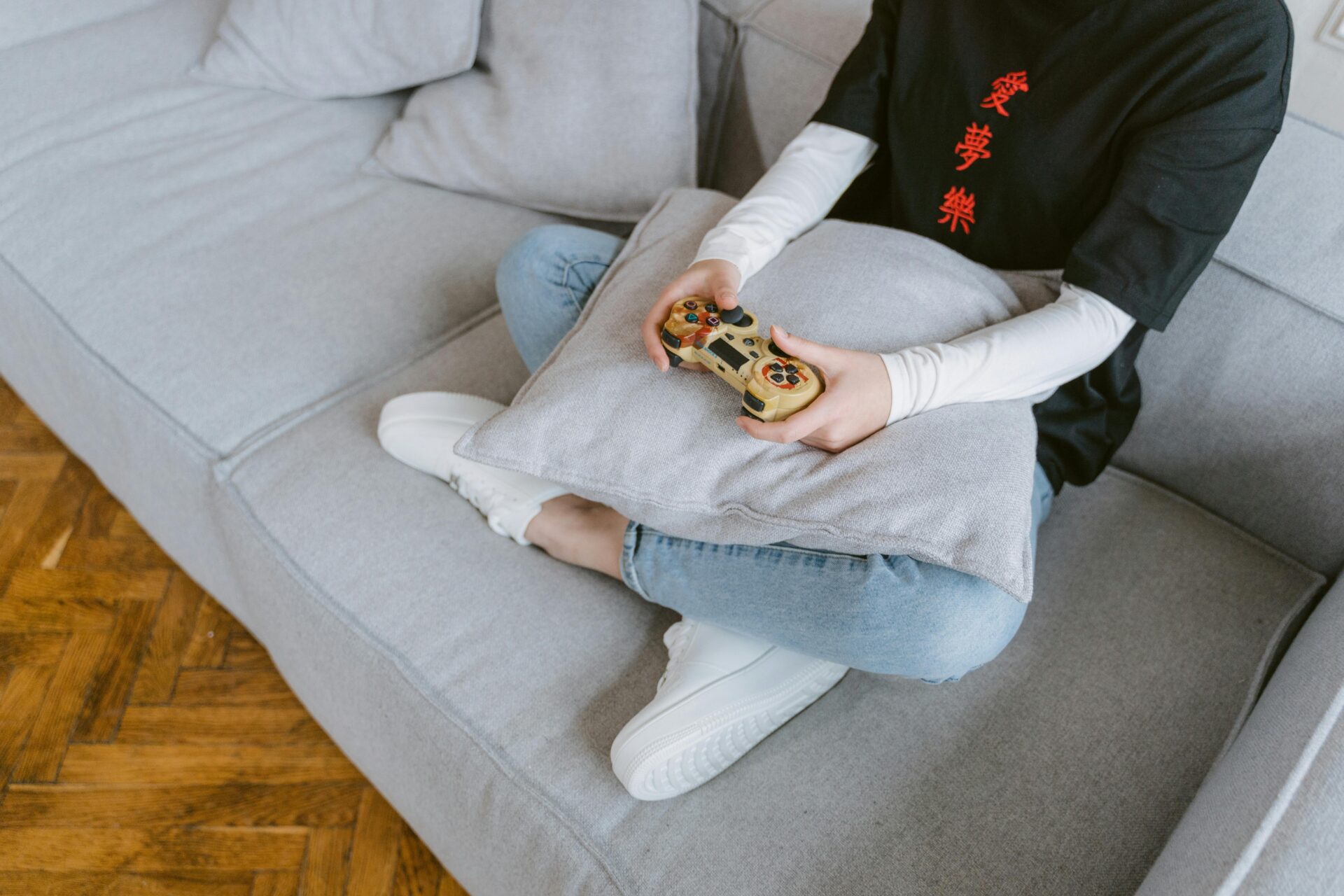 Person sitzt mit einem Controller auf einem grauen Sofa, von oben fotografiert.