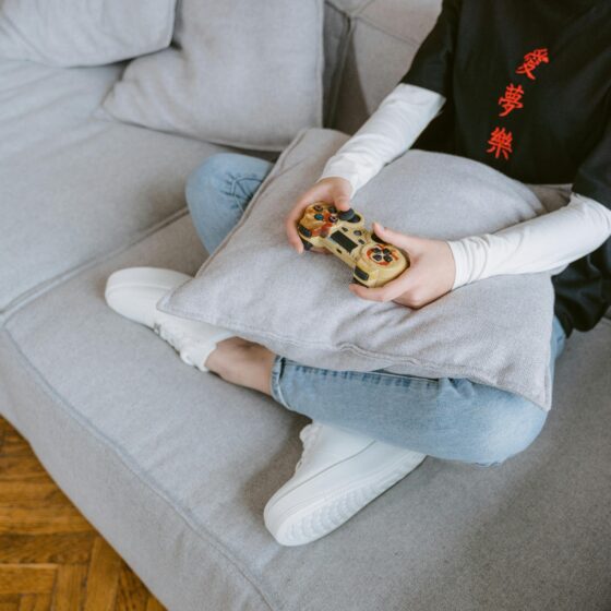 Person sitzt mit einem Controller auf einem grauen Sofa, von oben fotografiert.
